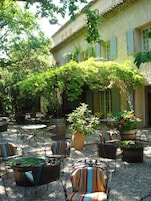 Un patio al aire libre con mesas y sillas, rodeado de vegetación y un edificio con ventanas.
