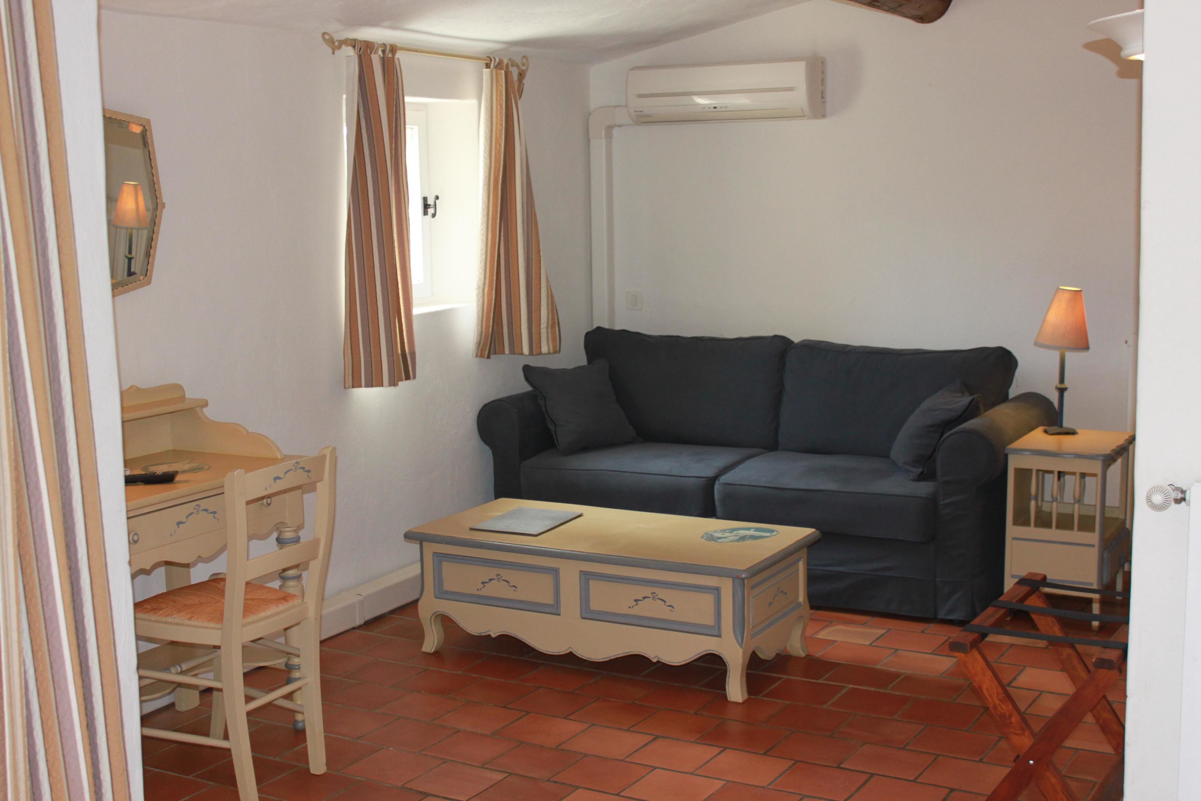 Une pièce avec un canapé bleu, une chaise en bois, une petite table, une lampe et un appareil de climatisation.