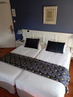 Habitación de hotel con una cama grande, dos almohadas, una mesita de noche con lámpara y un cuadro en la pared.