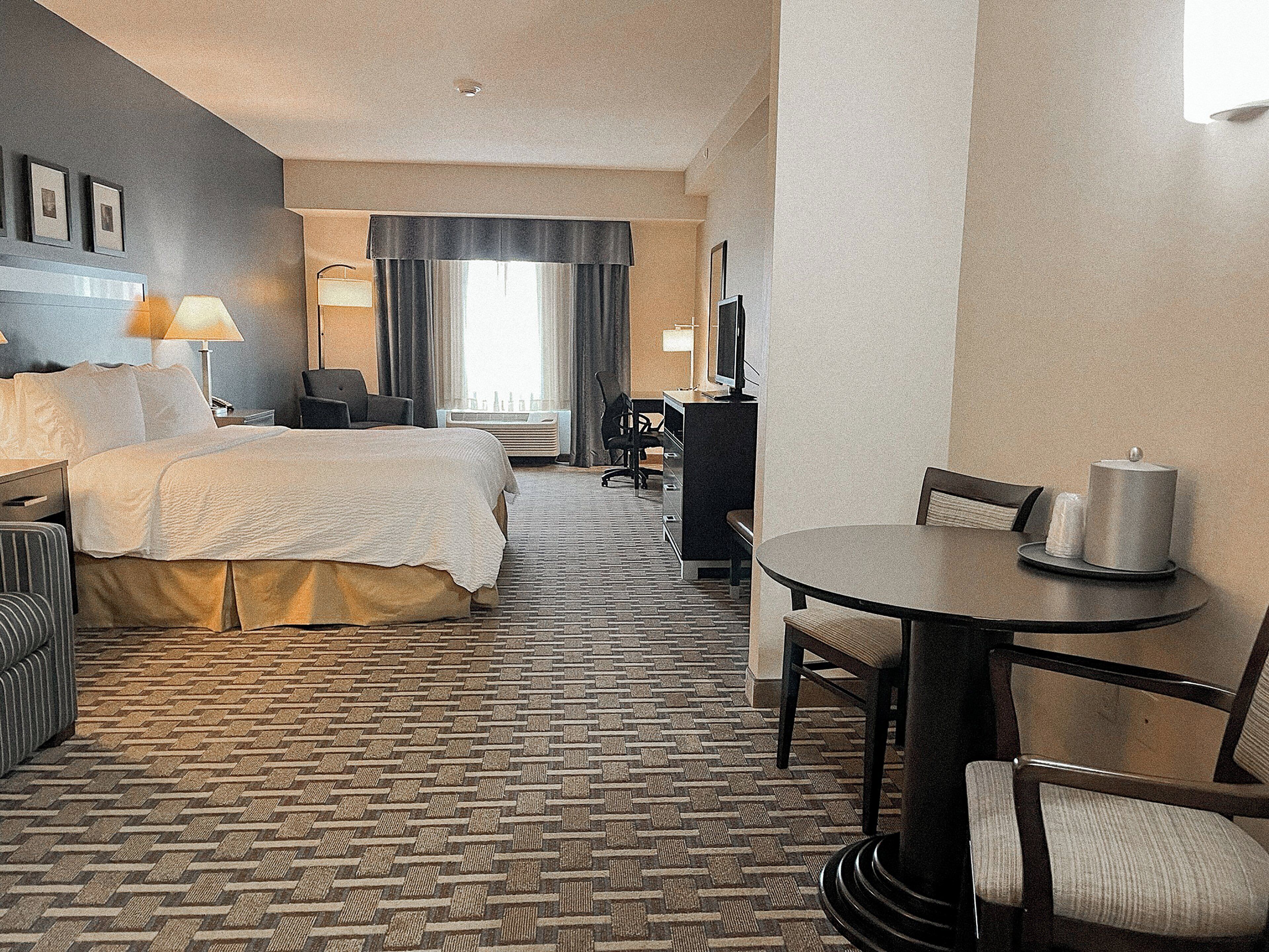 A hotel room with a bed, a desk, a chair, a table, and a TV.