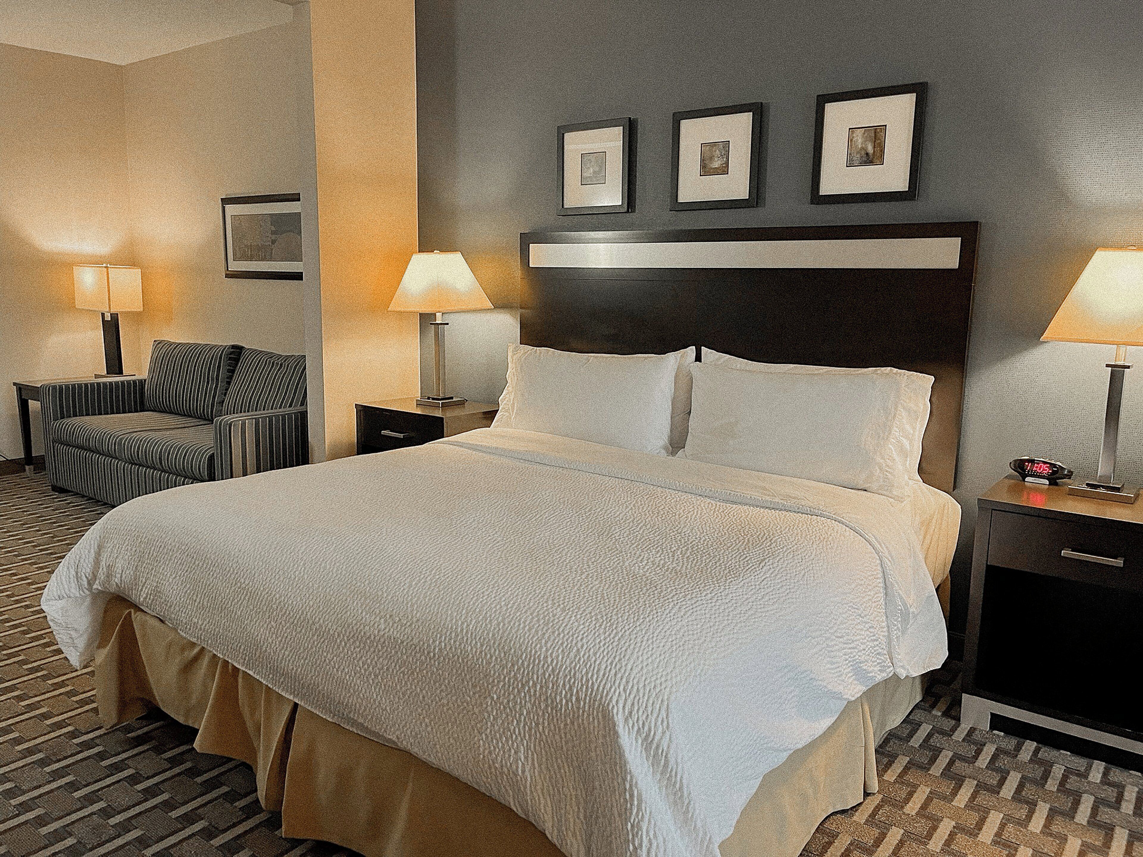 A hotel room with a large bed, two bedside tables with lamps, a chair, and framed pictures on the wall.