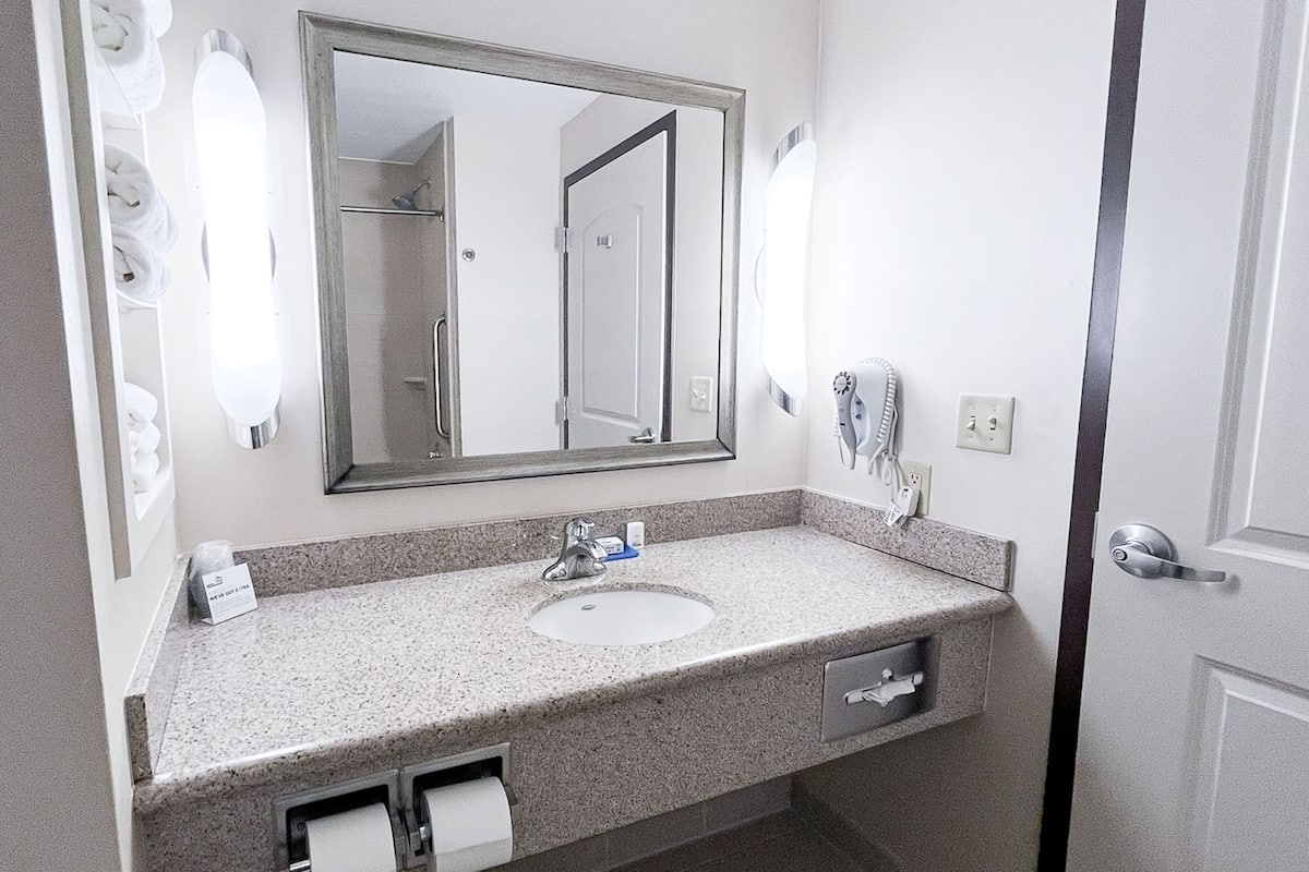 A bathroom with a sink, mirror, towel dispenser, and a hairdryer.