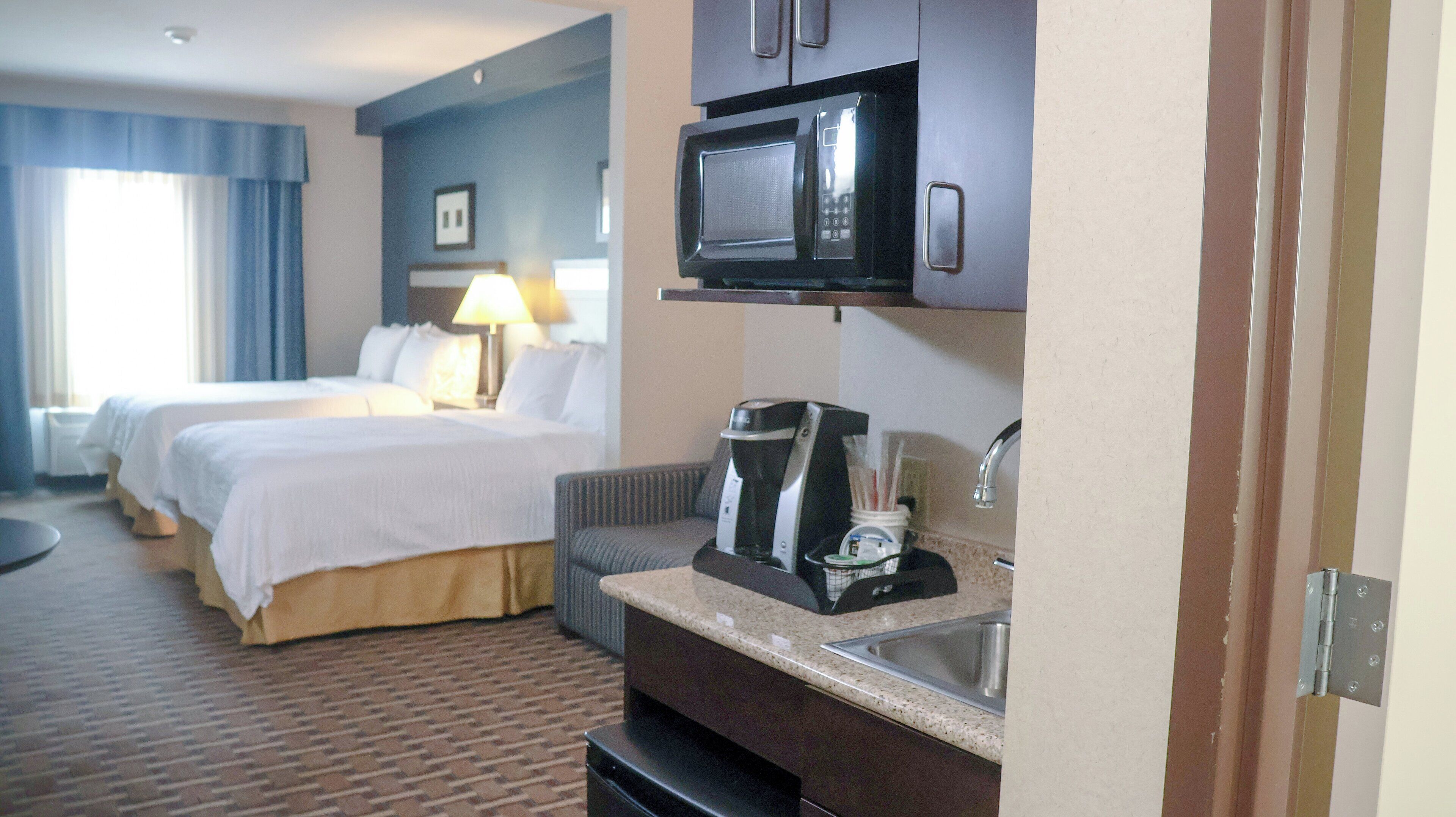 Een hotelkamer met twee bedden, een magnetron, een koffiezetapparaat en een wastafel.