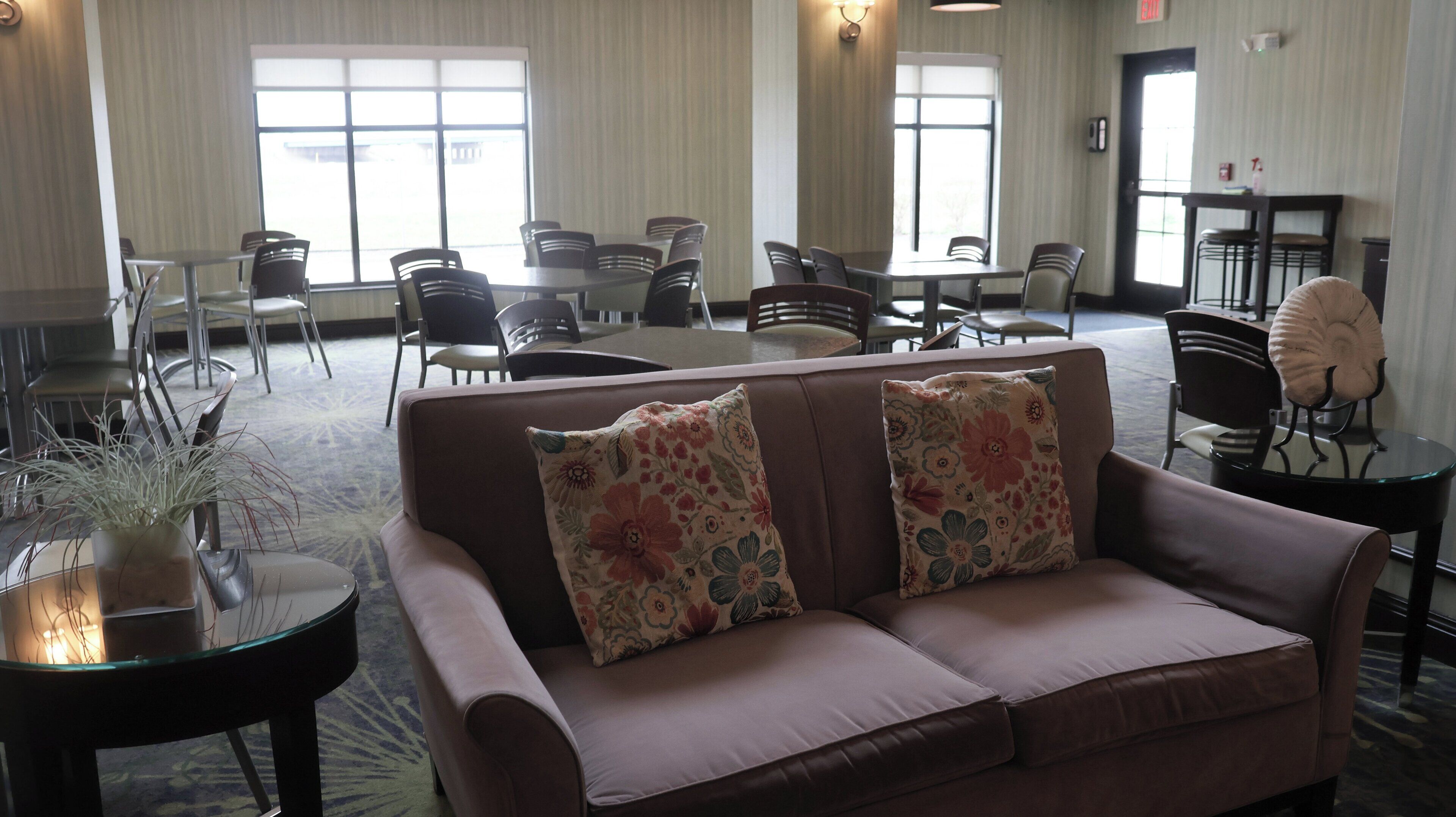 Eine Lobby mit einer braunen Couch, floralen Kissen, einem Glastisch mit einer Pflanze und mehreren Stühlen an Tischen.