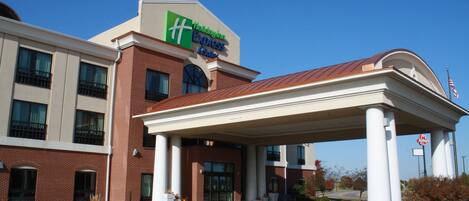 A hotel with a brick facade, a covered entrance, and a sign for the Hilton Express Suites.