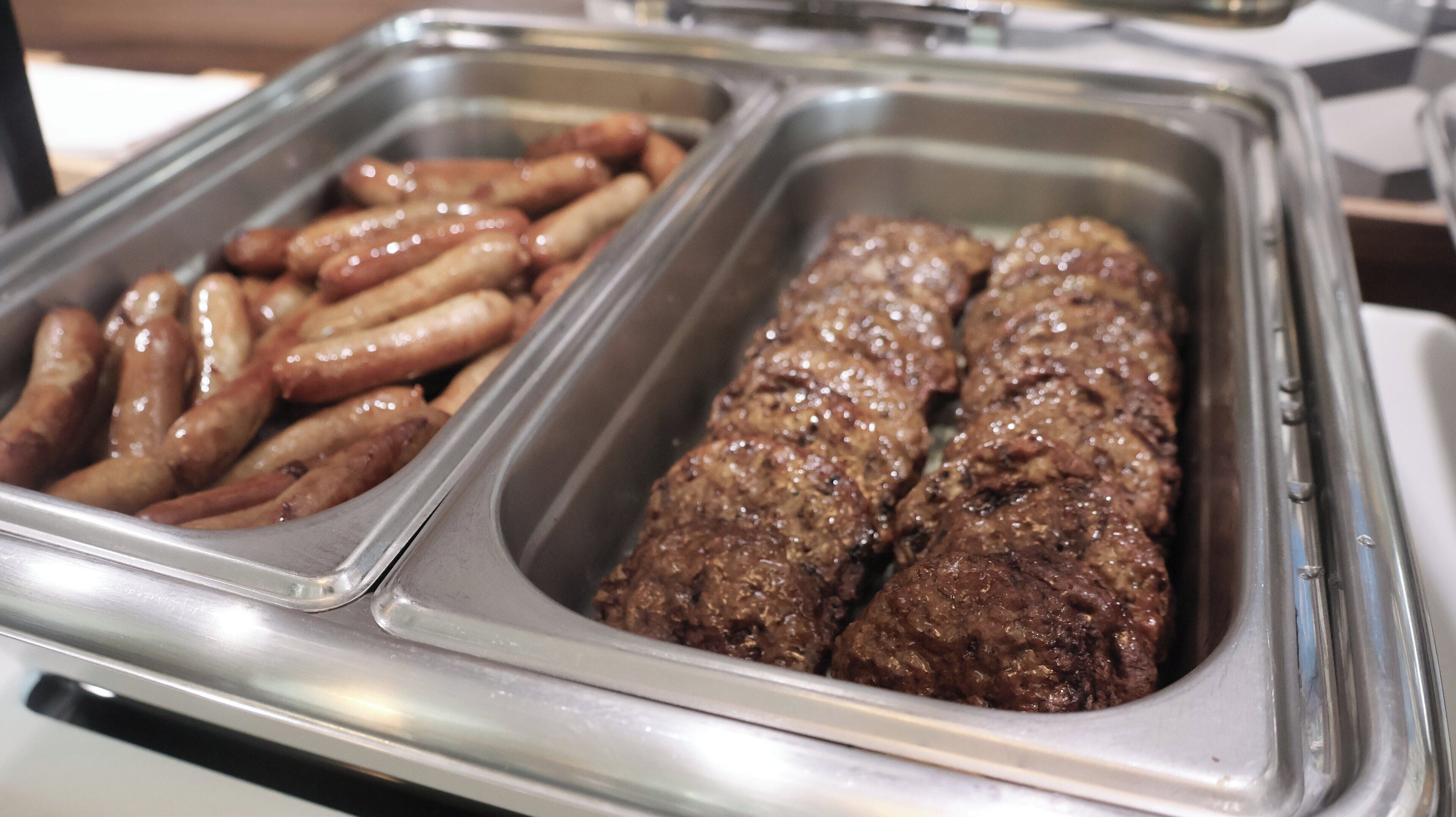 Un bufé con dos bandejas de comida: una con salchichas y la otra con albóndigas de carne.