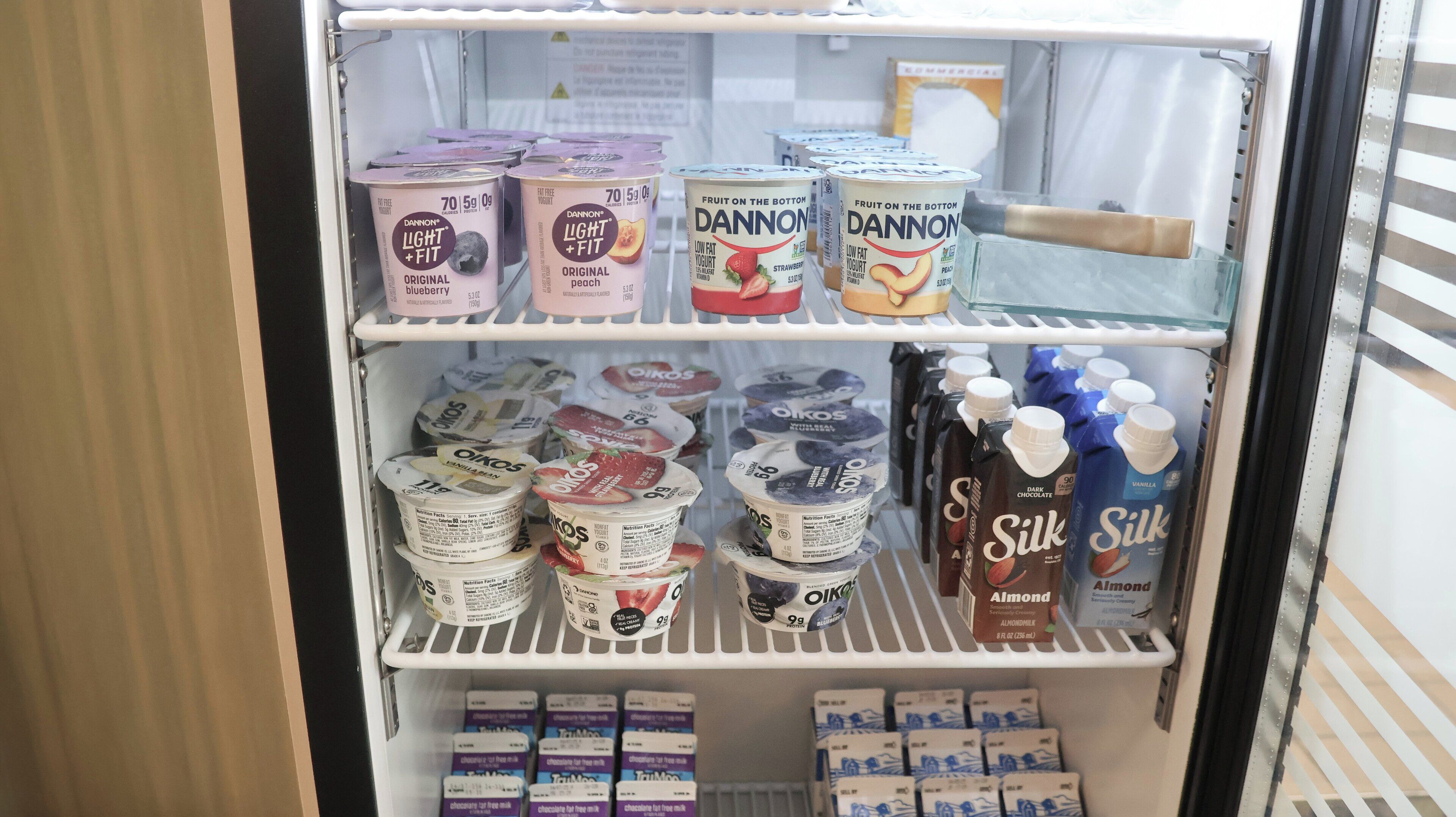 A refrigerated display with various dairy products including Dannon Light + Fit yogurt, Oikos yogurt, and Silk almond milk.