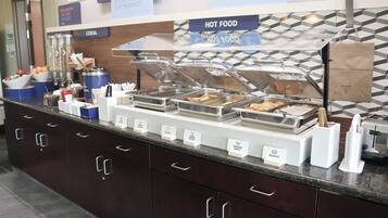 A buffet counter with labeled food sections including sausages, potatoes, cheese omelet, and biscuits.