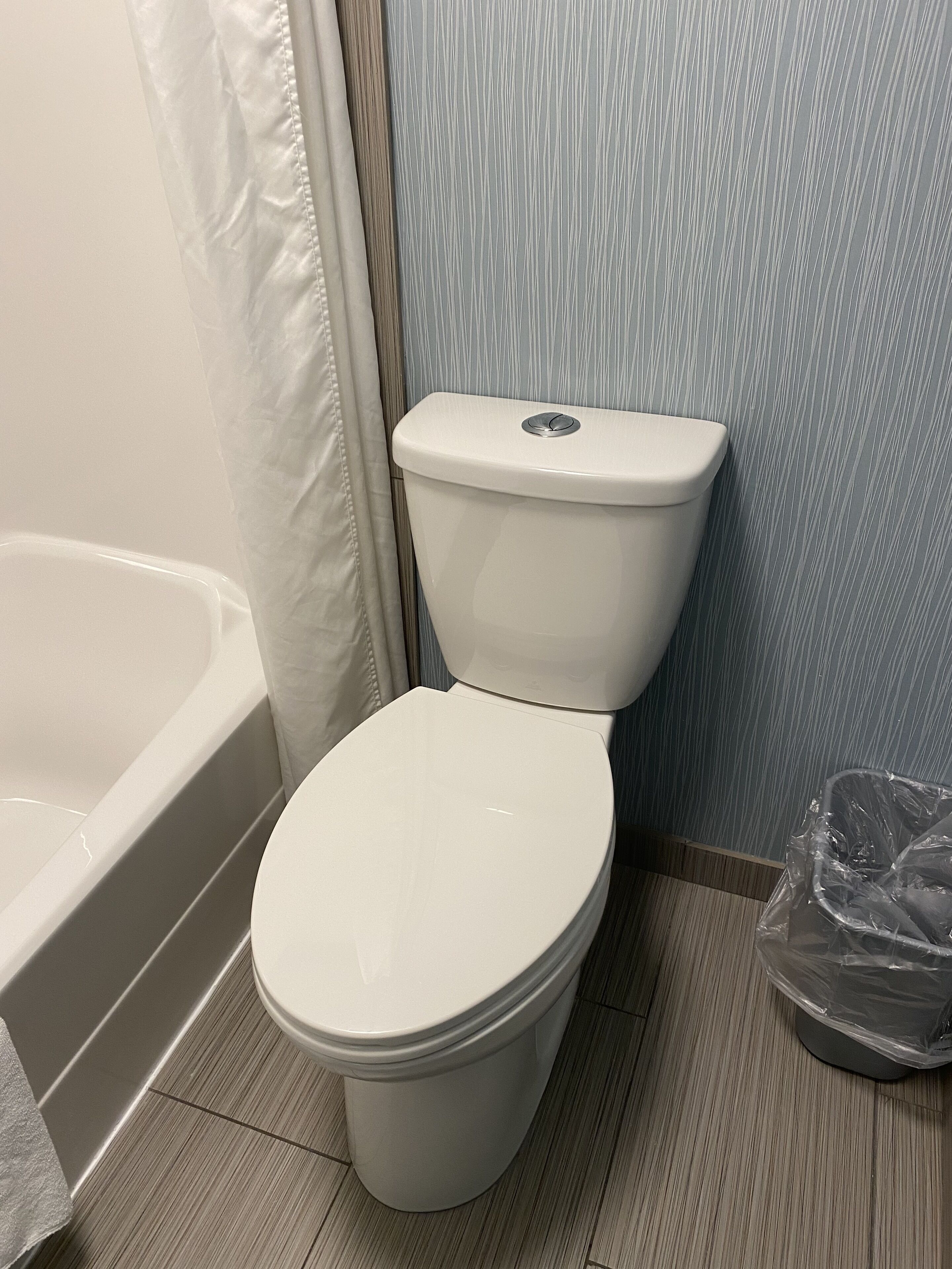 Eine weiße Toilette in einem Badezimmer mit einer Badewanne und einem Mülleimer.