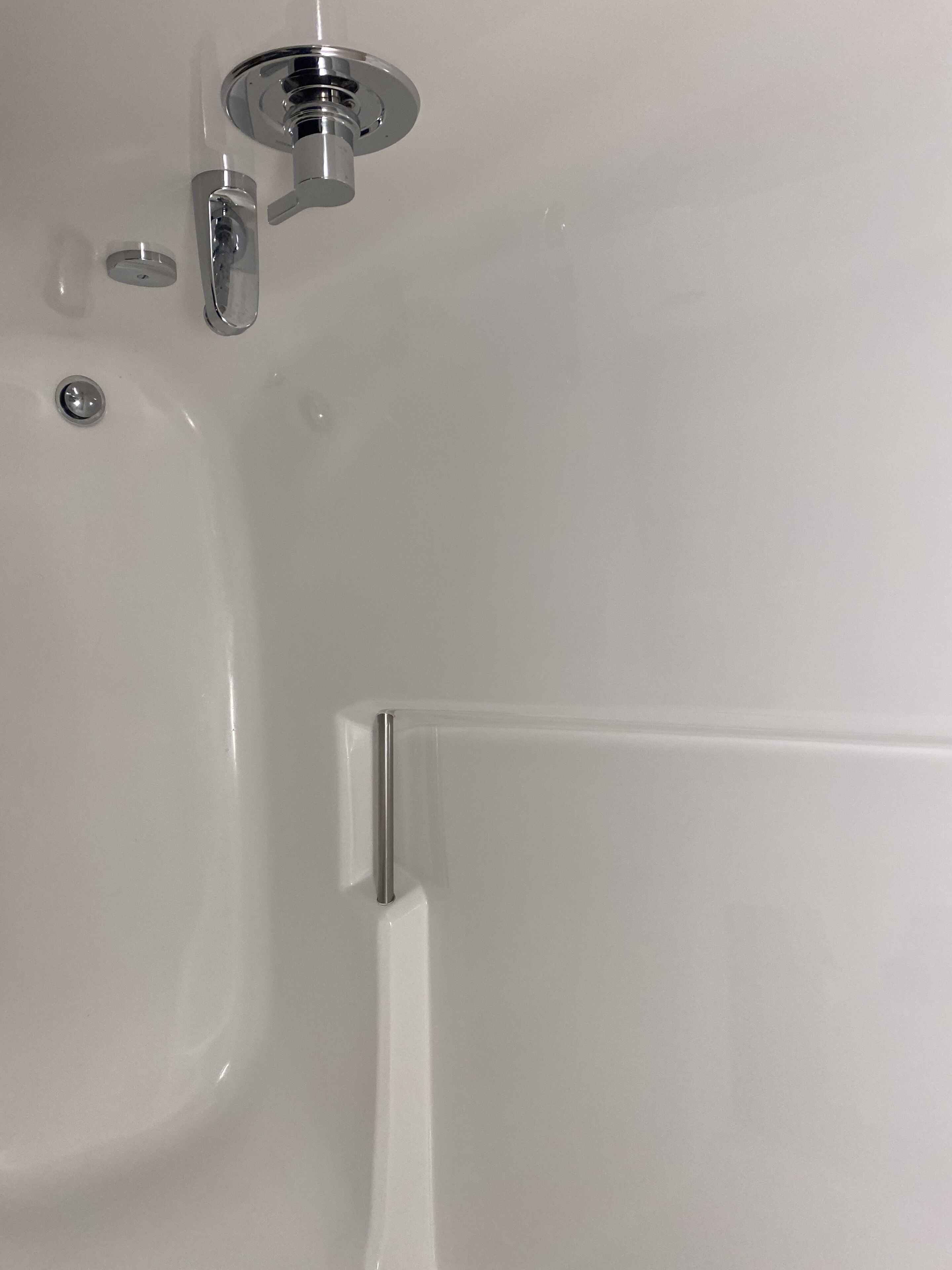 Une baignoire blanche avec un robinet chromé et un seul bouton chromé.