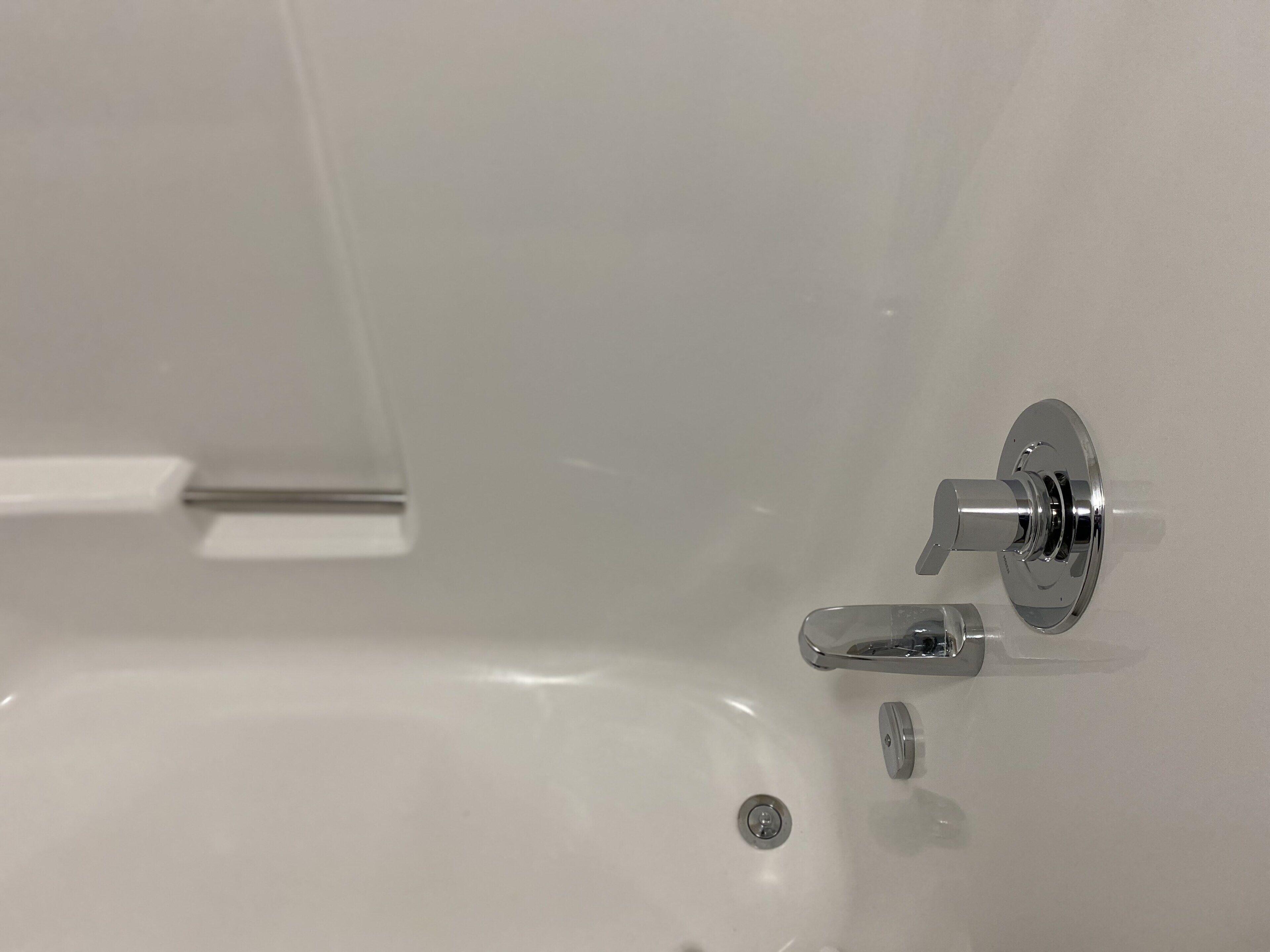 A bathroom with a white bathtub, a chrome faucet, and a visible drain.