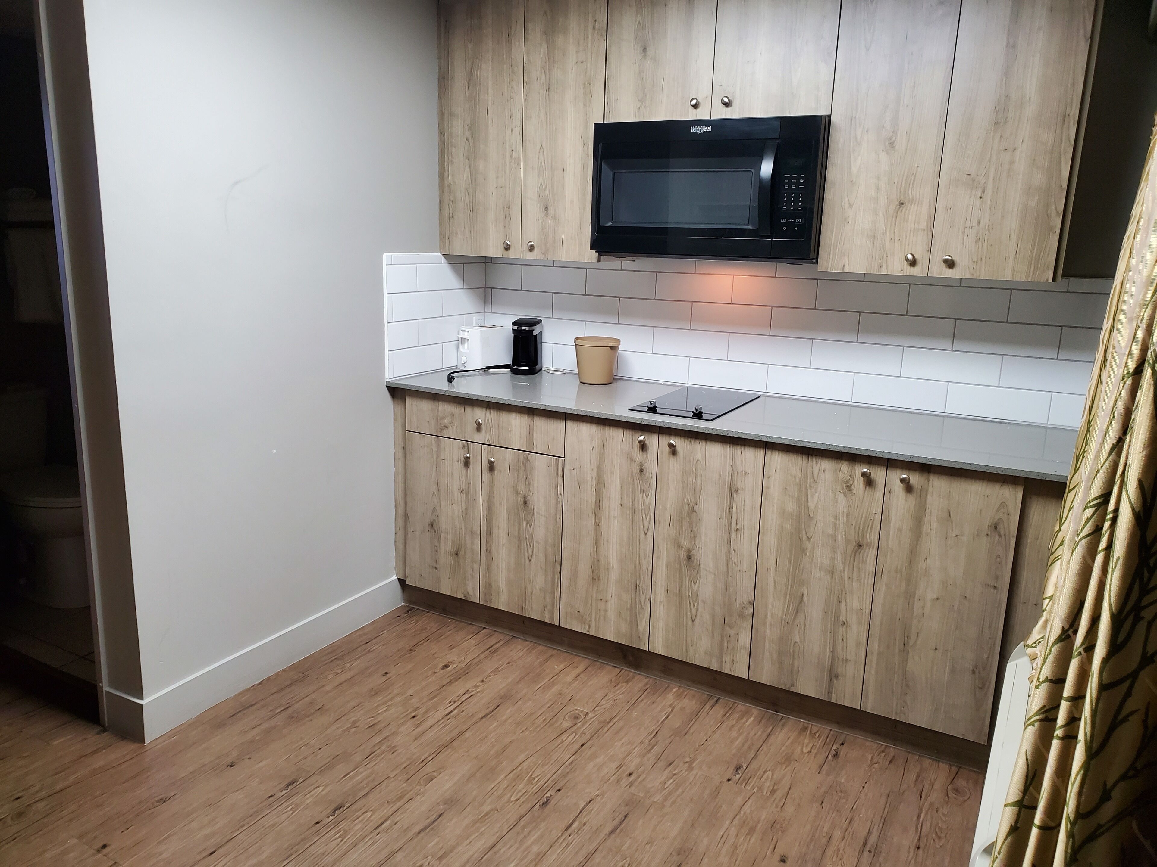 A modern kitchen with wooden cabinets, a black microwave, a coffee maker, and a toaster.