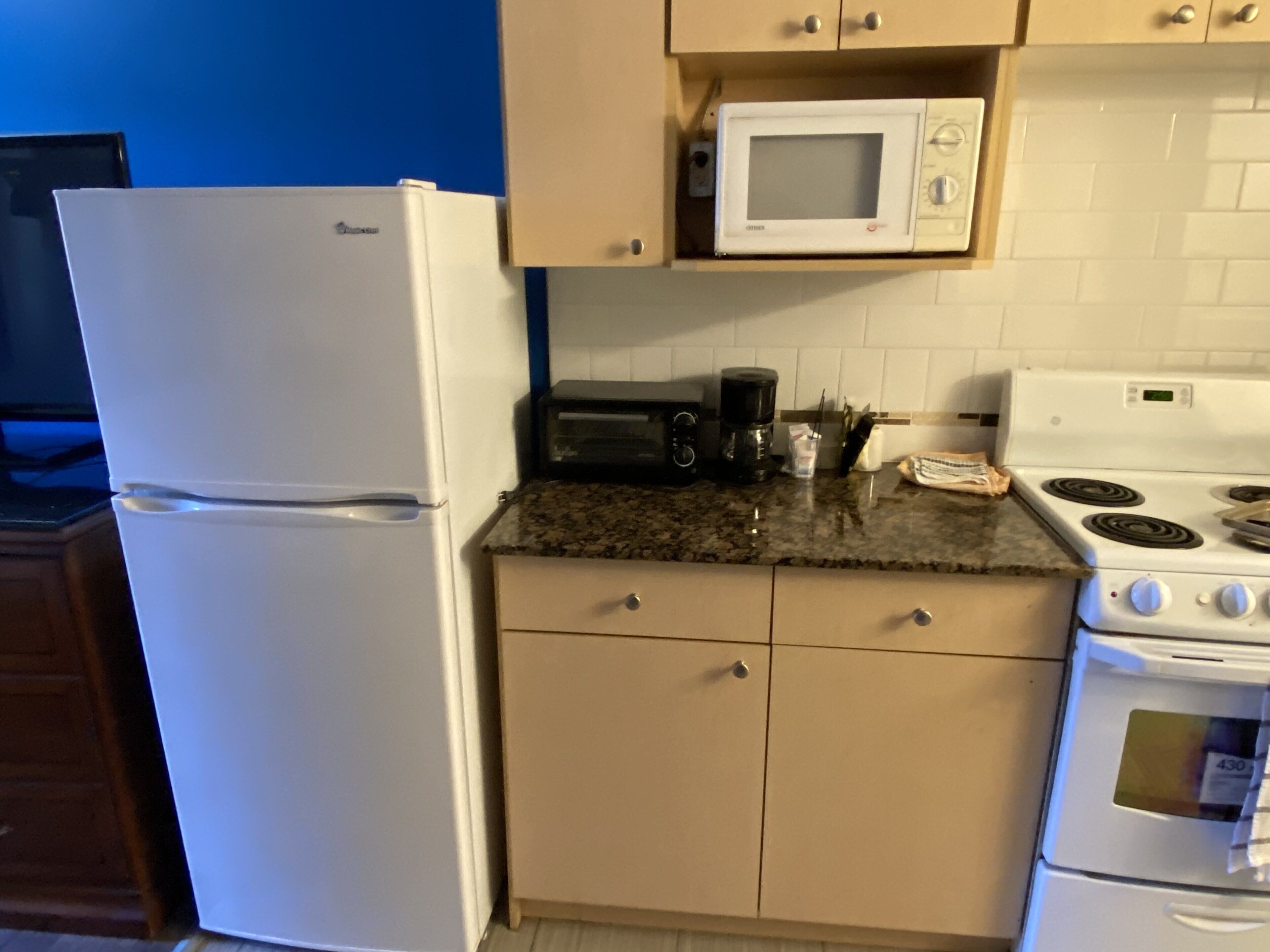 A compact kitchen with a refrigerator, microwave, toaster, coffee maker, and stove.