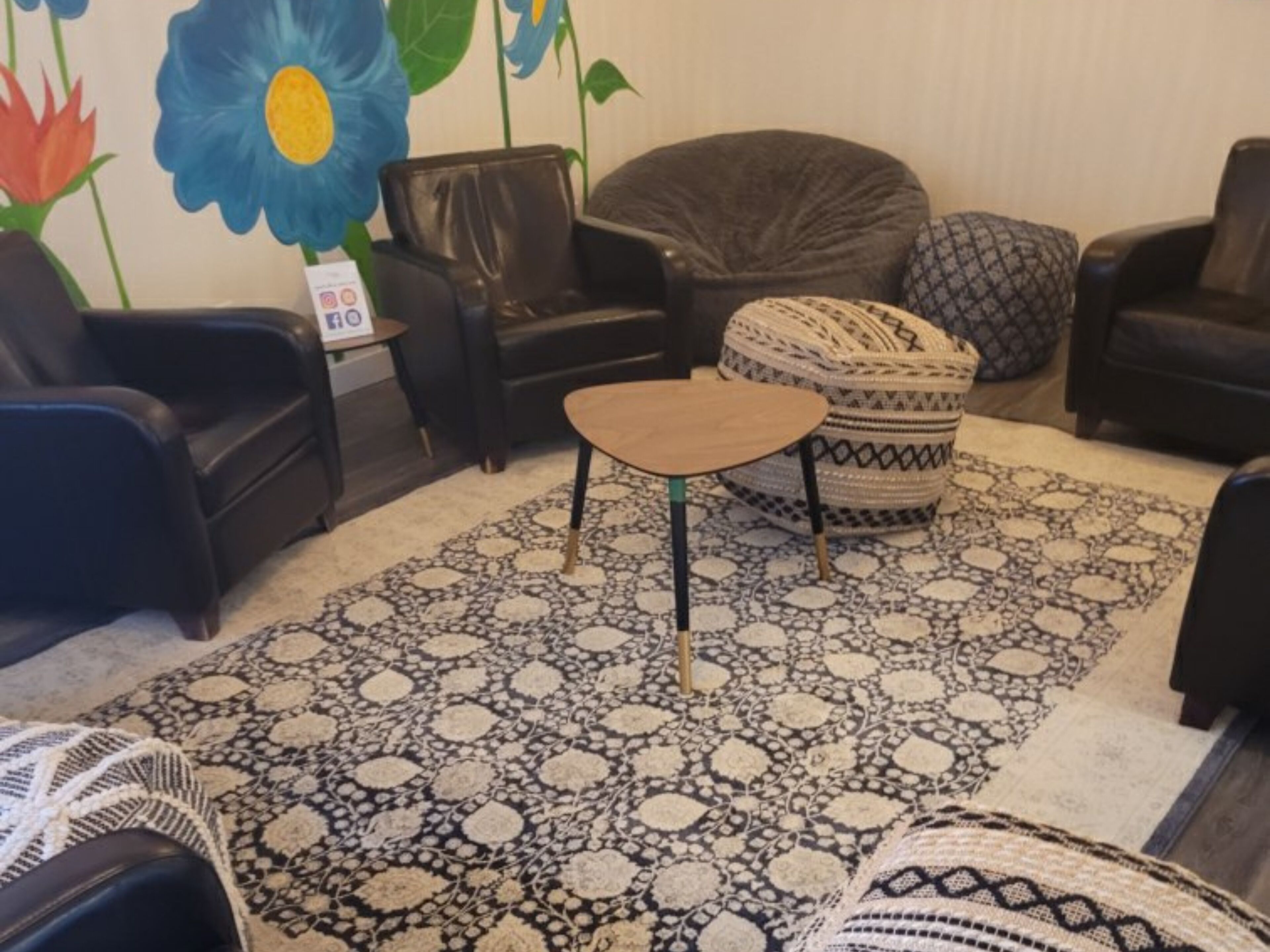 Una sala de estar acogedora con un tapete estampado, una mesita redonda y varios sillones de cuero negro.