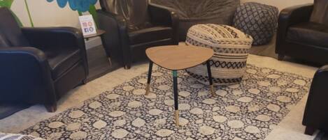 Una sala de estar acogedora con un tapete estampado, una mesita redonda y varios sillones de cuero negro.