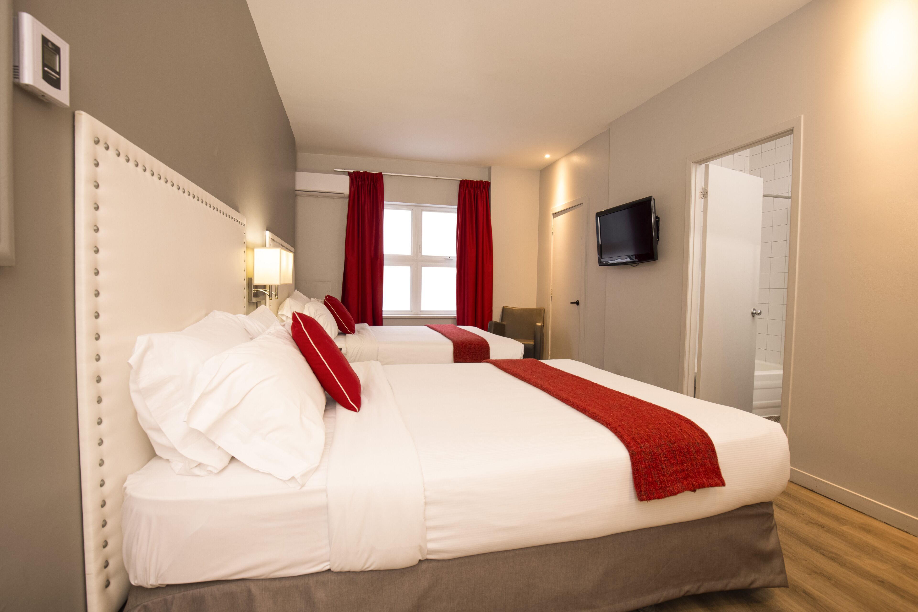 Una habitación de hotel con dos camas, un televisor y un ventanal con cortinas rojas.