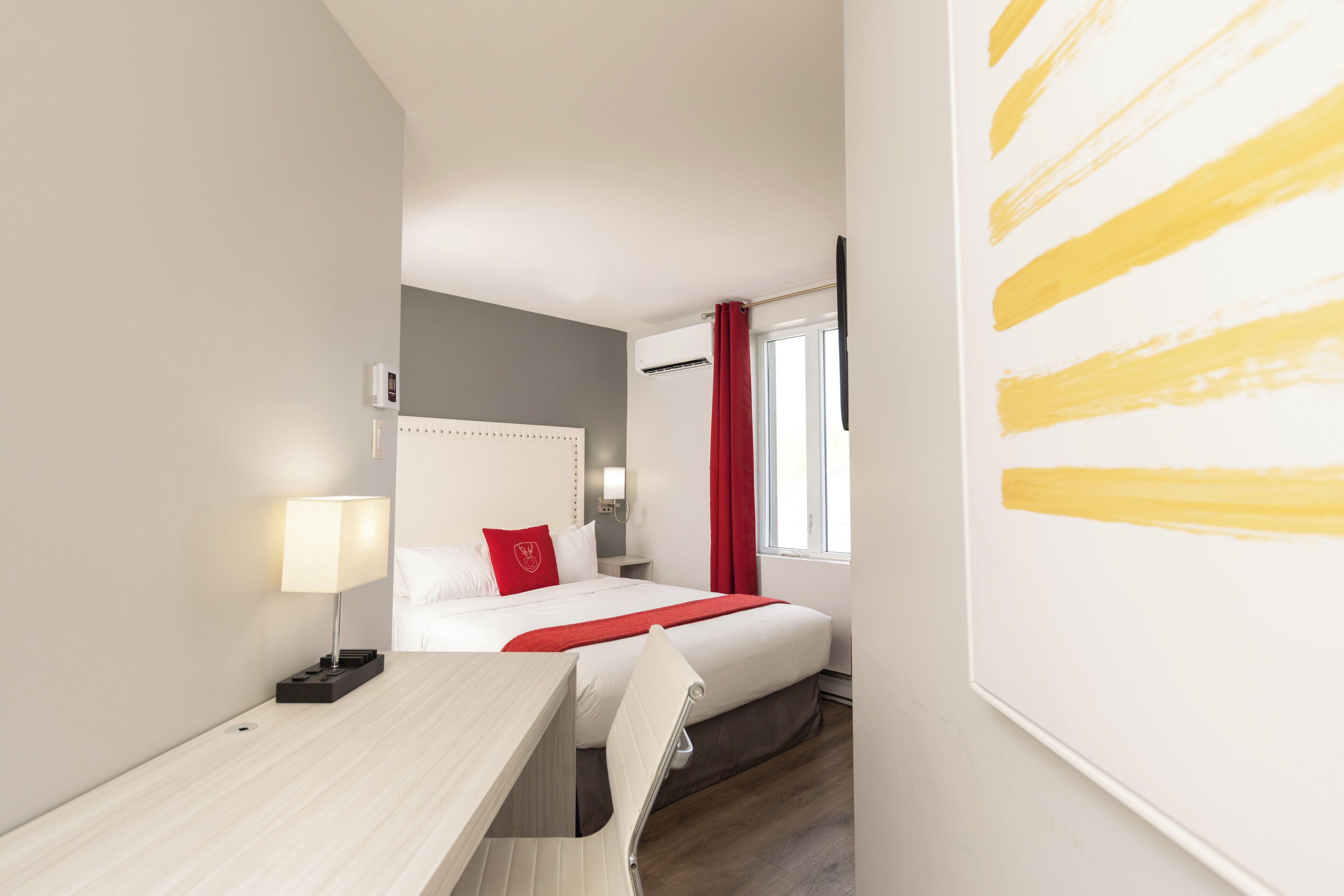 Quarto de hotel com cama, mesa de cabeceira, abajur e janela com cortinas.