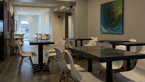 A modern dining area with wooden flooring, white chairs, and black tables. There is a large painting on the wall and a door leading outside. - Hôtel du Nord (Québec City)