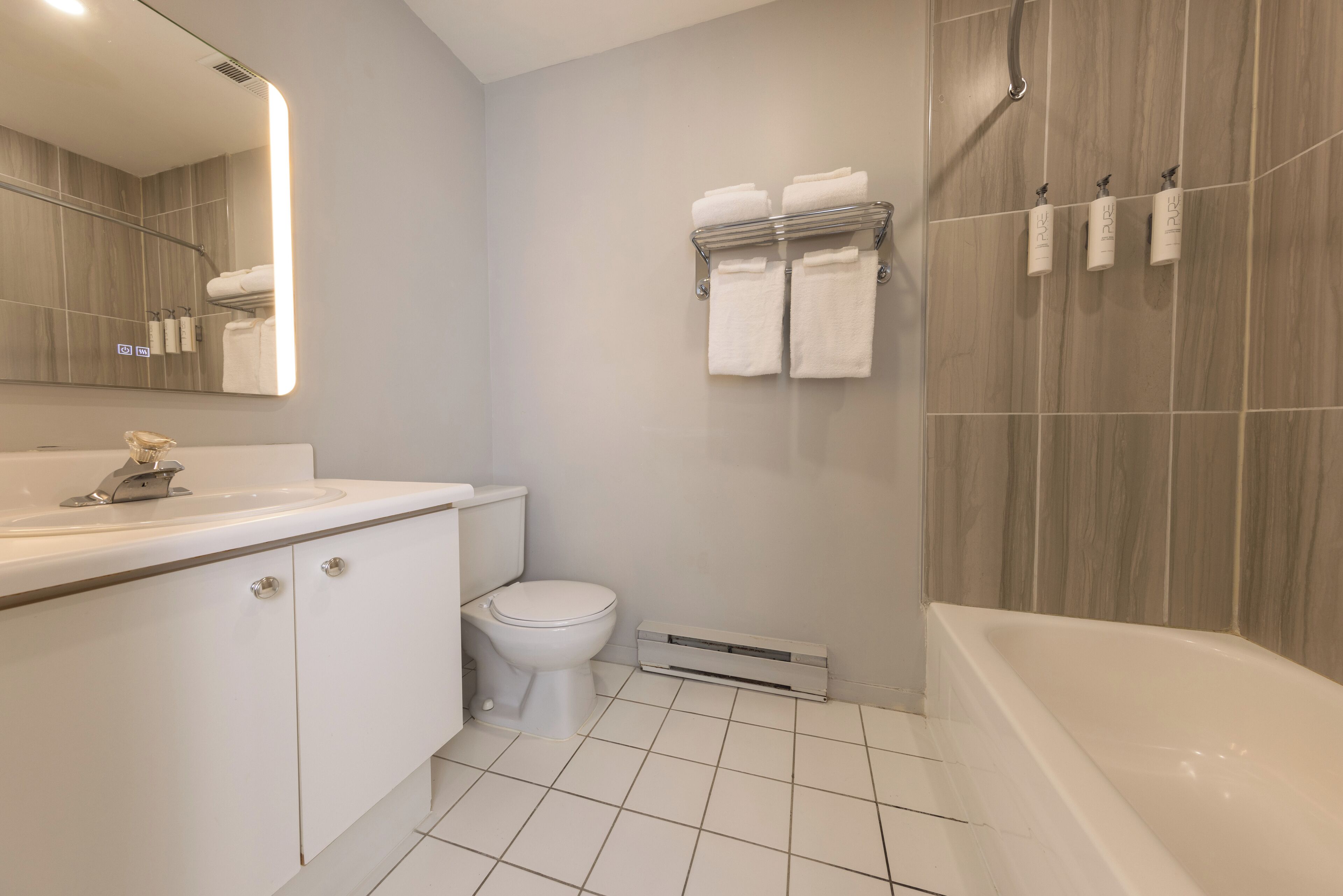 A modern bathroom with a white sink, toilet, and bathtub. There are three towel racks on the wall, and a mirror above the sink.