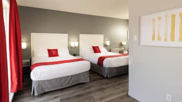 Une chambre d’hôtel avec deux lits, chacun agrémenté d’un coussin rouge, d’une literie blanche et d’une couvre-lit grise. On y trouve des lampes de chevet et une œuvre d’art encadrée au mur.