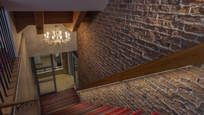 A staircase with red carpet, a brick wall, and a chandelier. - Hôtel du Nord (Québec City)