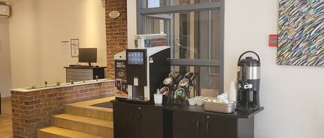Un vestíbulo de hotel con una estación de café, una recepción y una escalera que sube a los pisos superiores.