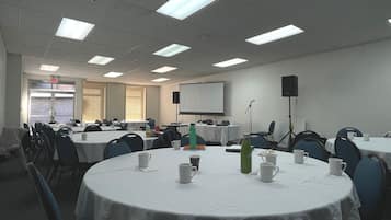 Un salón de conferencias con mesas redondas, sillas, una pantalla de proyector y una pizarra.