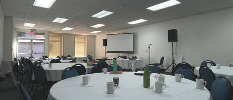 A conference room with round tables, chairs, a projector screen, and a whiteboard.