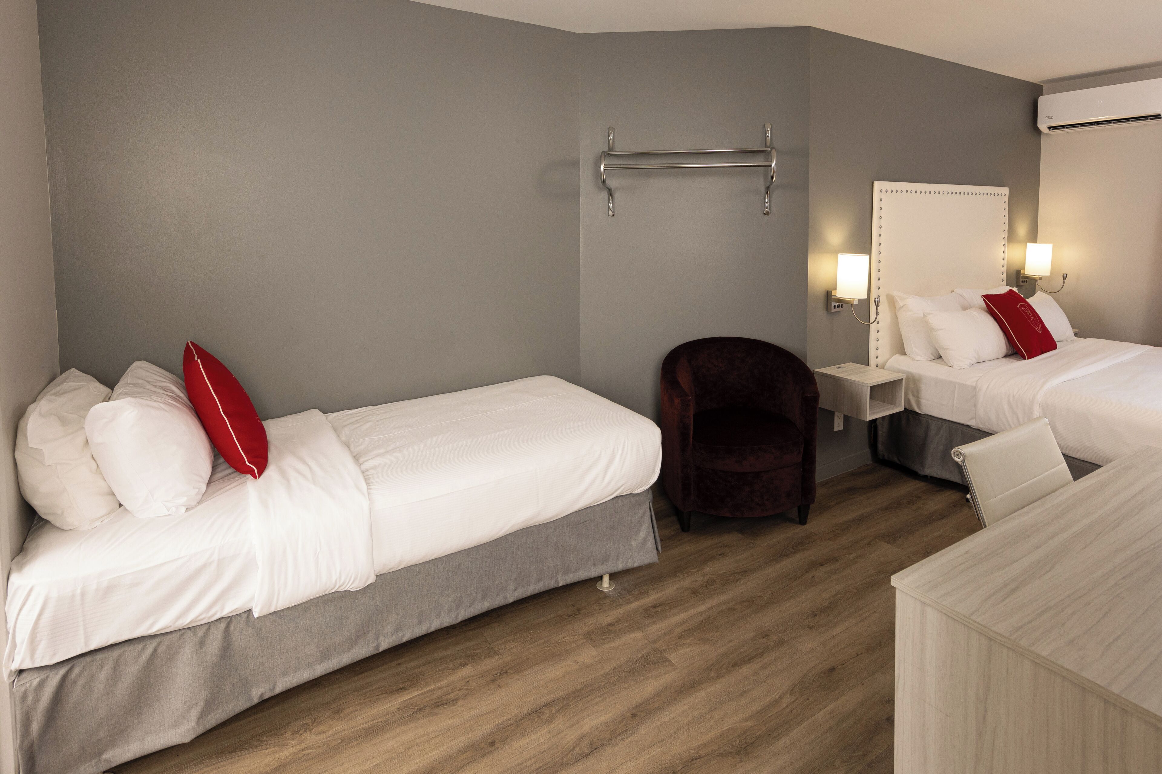 A hotel room with two beds, a chair, a bedside table, and a wall-mounted towel rack.
