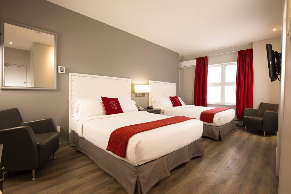 A hotel room with two beds, a mirror, a desk, and a chair.