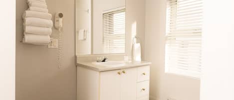 Un baño con tocador blanco, un espejo, toallero y secador de pelo.