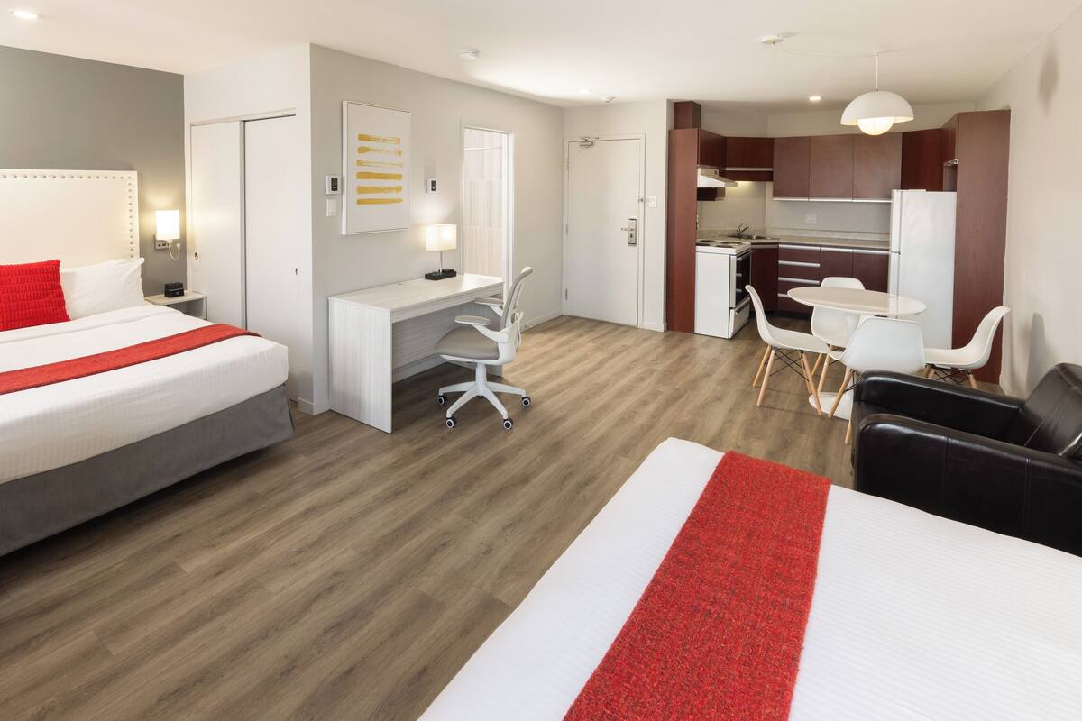 A hotel room with a bed, desk, chair, and kitchenette.