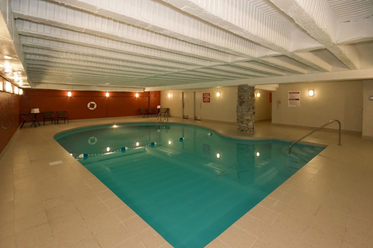 An indoor swimming pool with a stone pillar, lounge chairs, and a tiled floor.