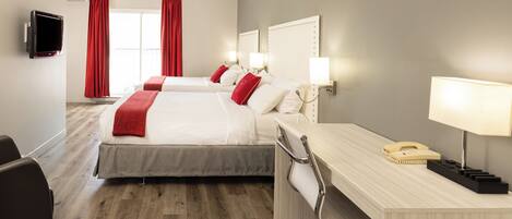 A hotel room with two beds, a desk with a telephone, and a television on the wall.