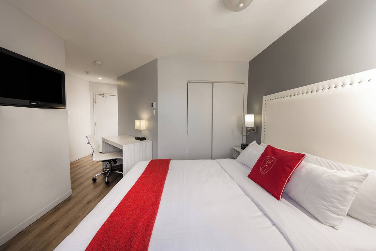 A modern hotel room with a large bed, a desk, and a flat-screen TV.