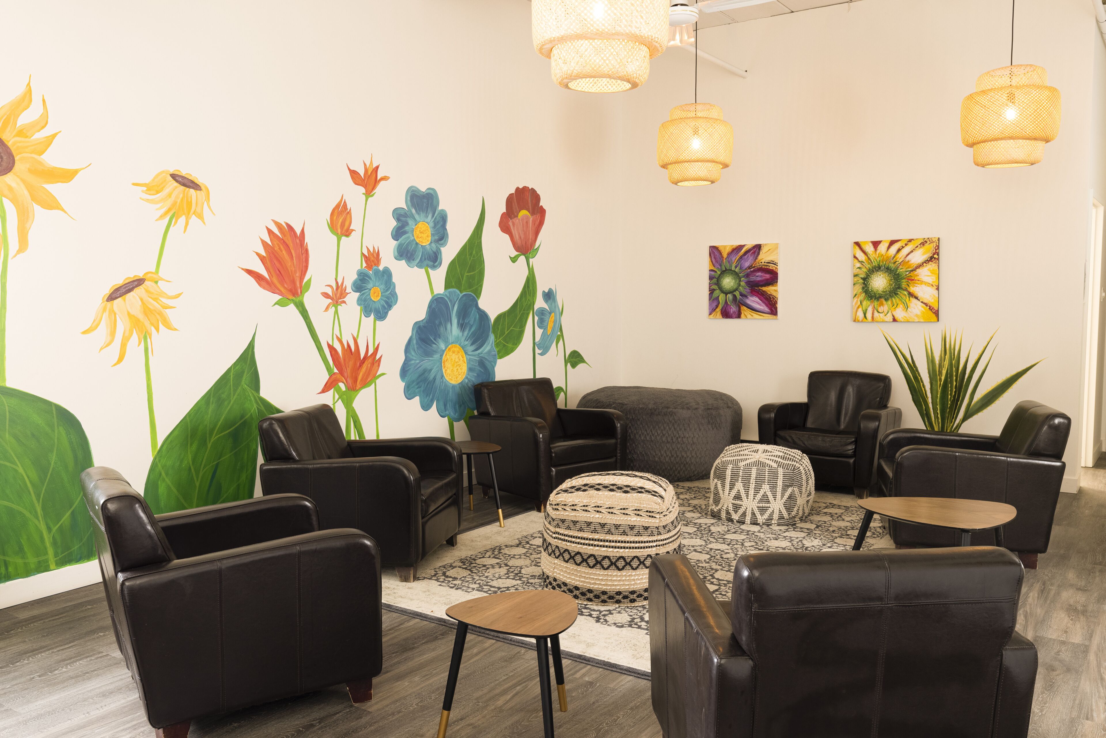 Un área de estar moderna con sofás de cuero negro, una alfombra estampada y un gran mural floral en la pared.