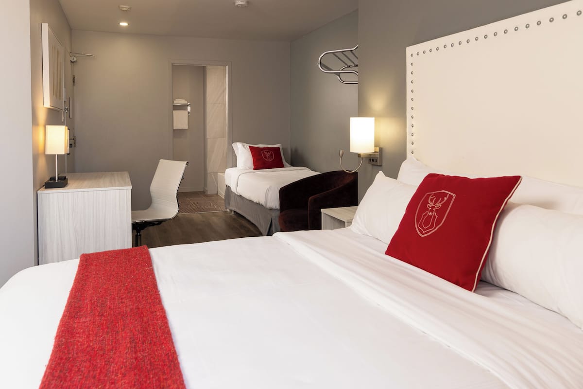 A hotel room with a large bed, two smaller beds, a desk, and a chair.
