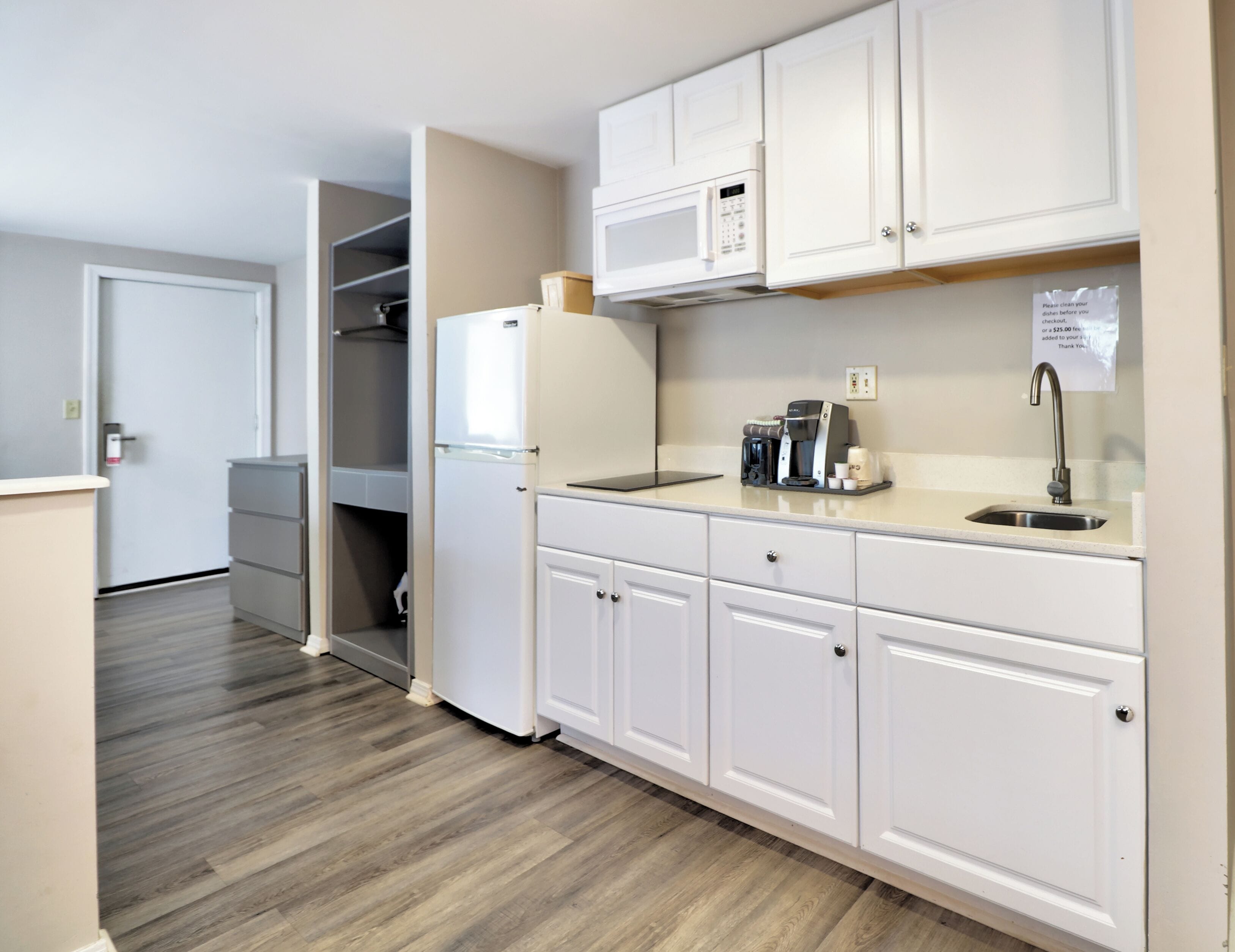 Una cocina moderna con armarios blancos, microondas integrado, cafetera y pileta.