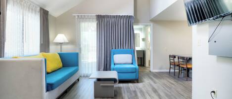 A modern living room with a sofa, armchair, coffee table, and a flat-screen TV mounted on the wall.