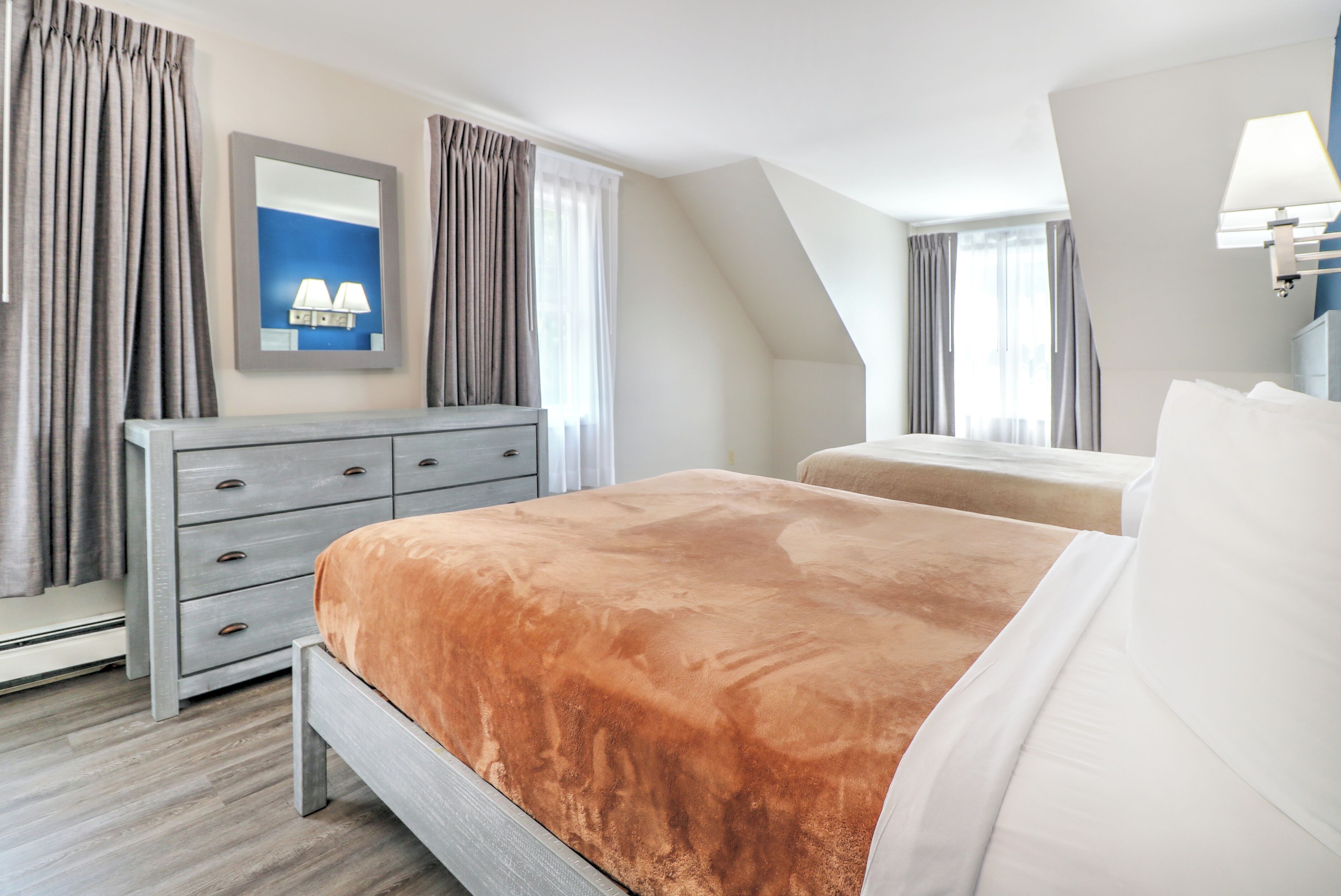 Una habitación de hotel con cama, cómoda, espejo y ventana con cortinas.