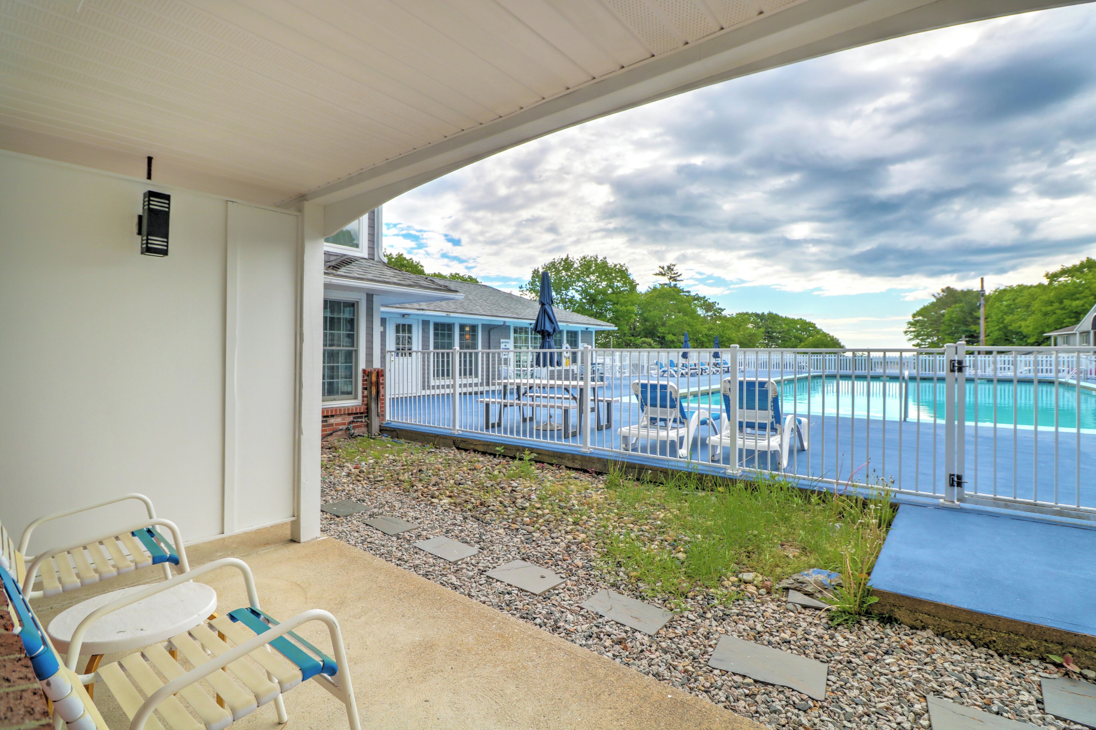 A covered outdoor area with a pool, lounge chairs, and a building in the background.