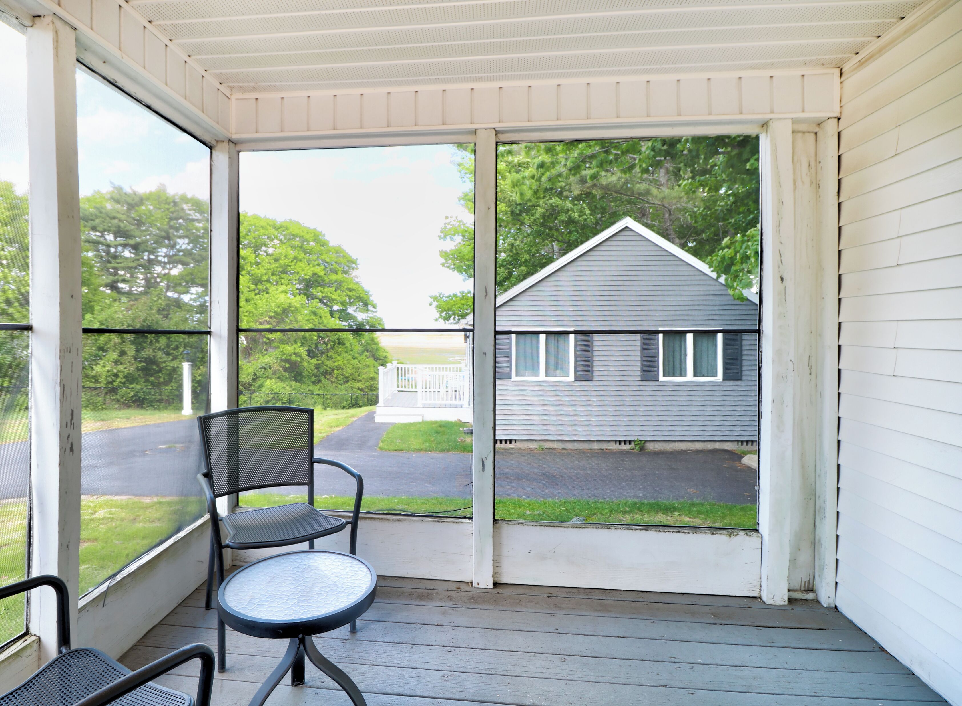 A covered porch with a table and chairs, a view of a house, and a pathway leading to a fence.