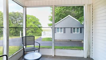 A covered porch with a table and chairs, a view of a house, and a pathway leading to a fence.