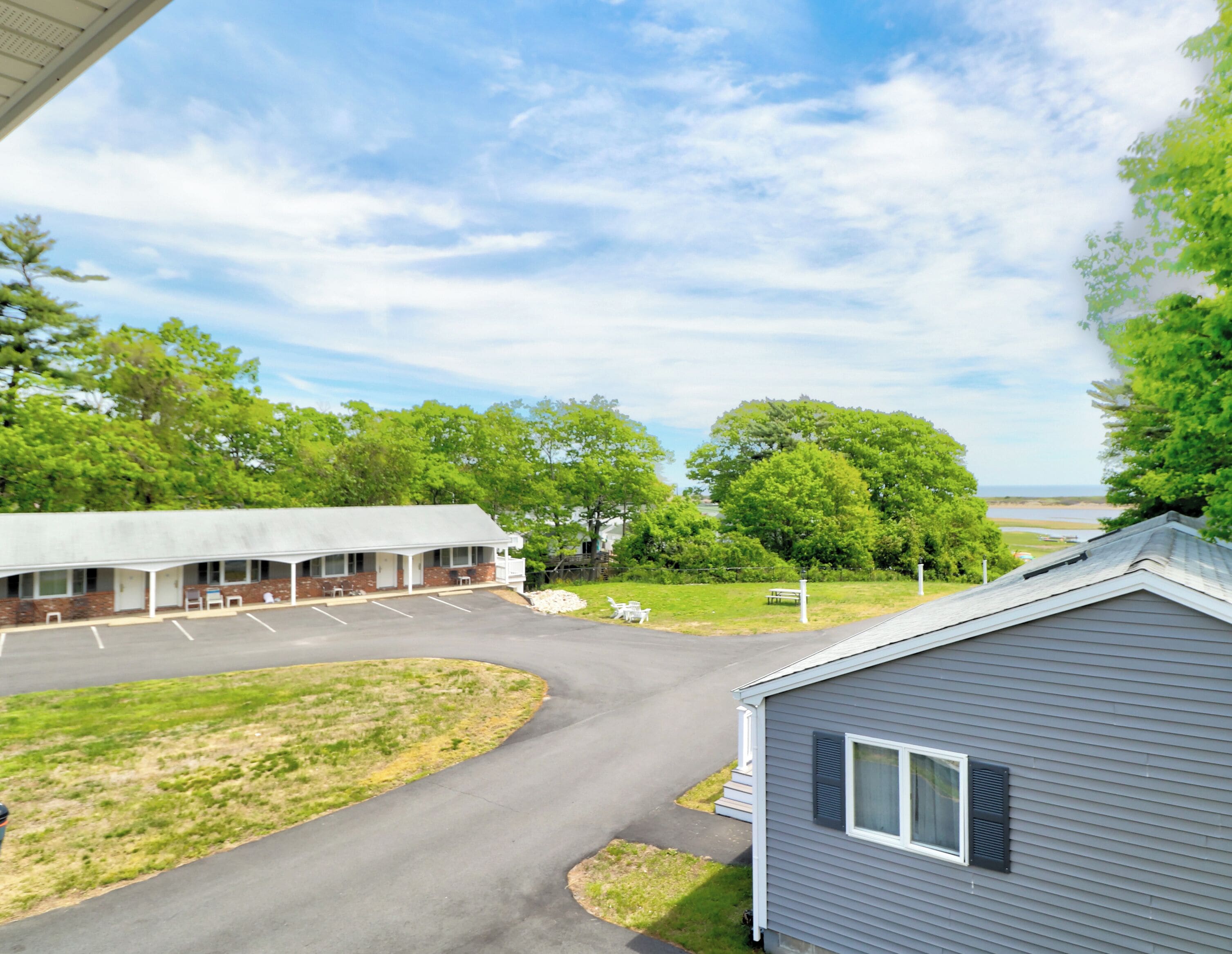 A motel with a parking lot, a covered outdoor seating area, and a view of a body of water.