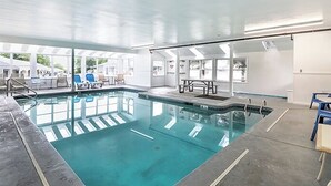 Une piscine intérieure à l’eau claire, entourée de chaises longues et de tables, et dotée de grandes fenêtres laissant entrer la lumière naturelle.