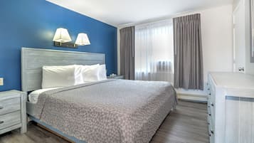 Habitación de hotel con cama, mesitas de noche, cómoda y ventana con cortinas.