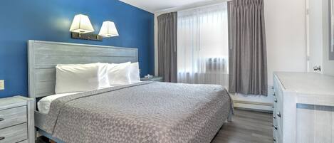 A hotel room with a bed, bedside tables, a dresser, and a window with curtains.