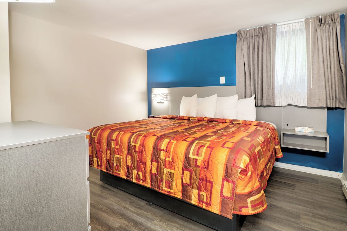 A hotel room with a bed, a bedside table, a wardrobe, and a window with curtains.