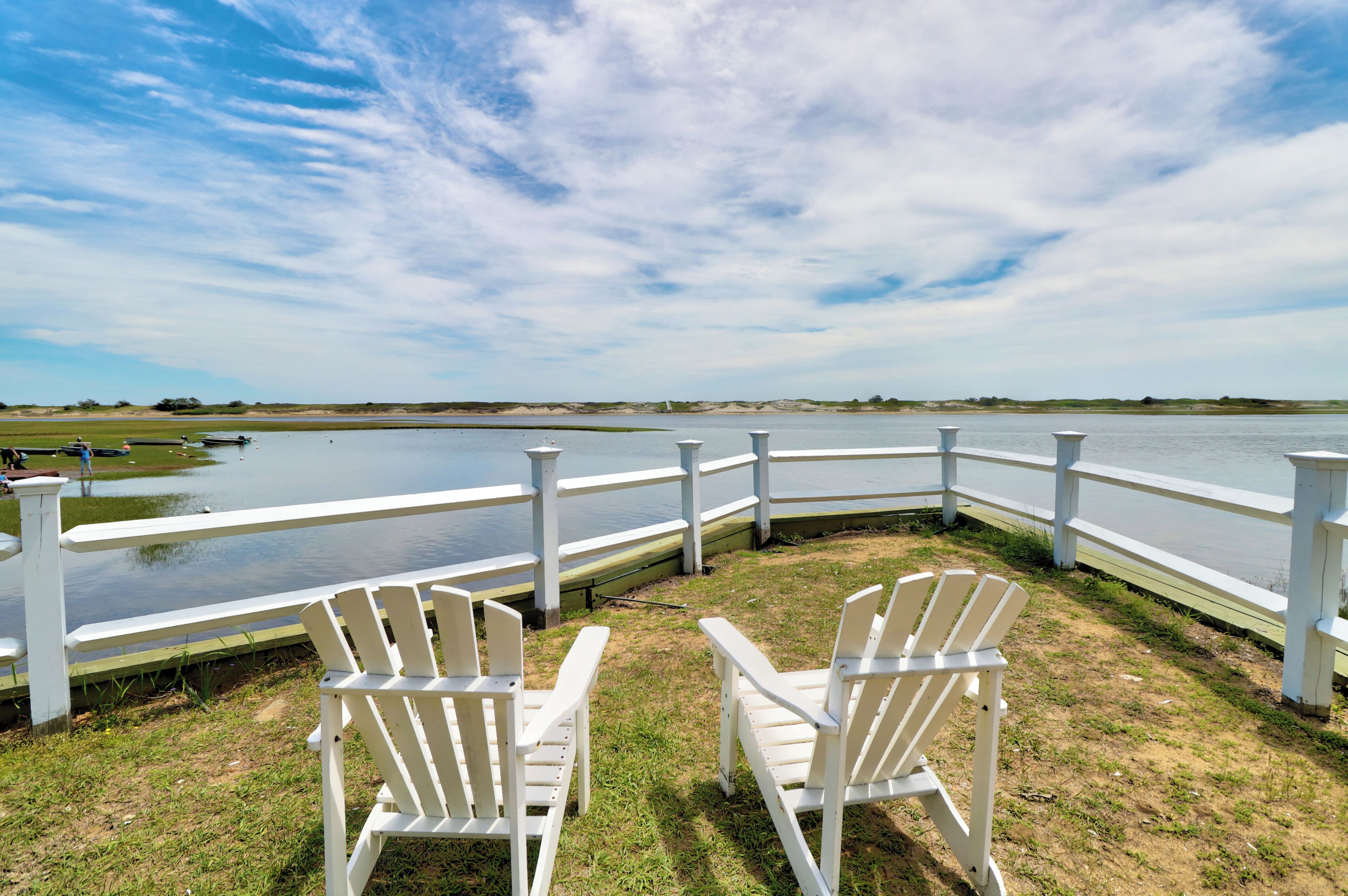 A lakeside view with white Adirondack chairs and a white fence overlooking the water.