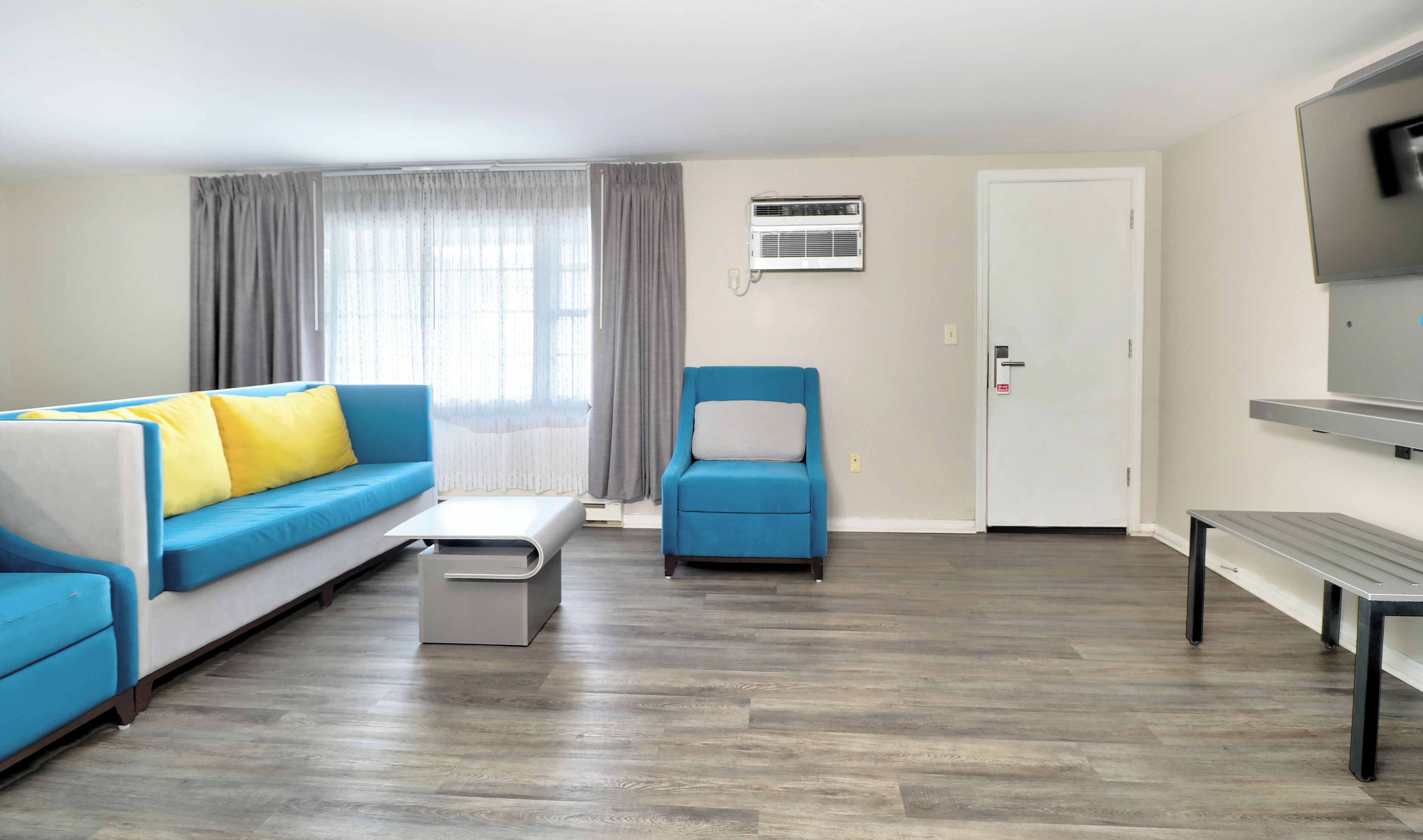 Een moderne woonkamer met een blauwe bank, een bijpassende fauteuil, een bijzettafeltje en een aan de muur bevestigde televisie.